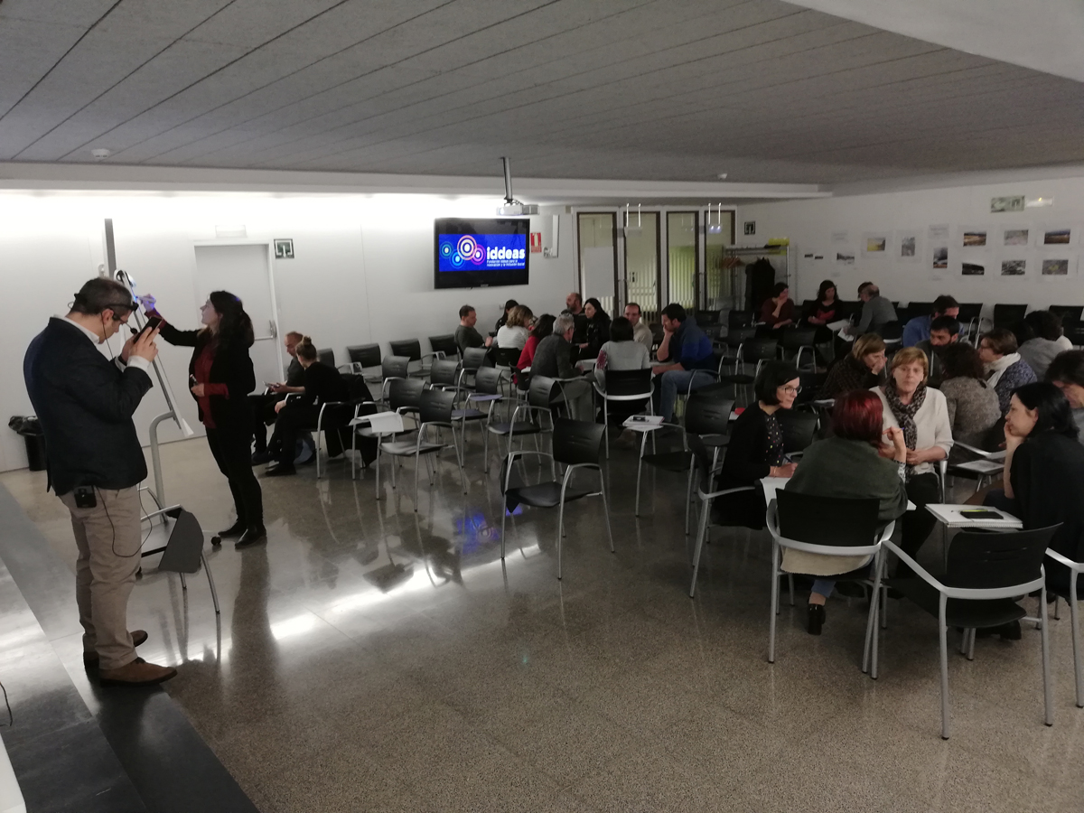 Imagen de la formación en el departamento de desarrollo rural del Gobierno de Navarra. Las personas están sentadas en grupos, mientras un ponente consulta su teléfono móvil y otra ponente escribe en una pizarra.