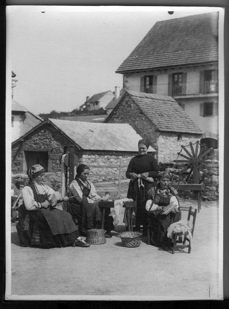 Fotografía en blanco y negro en la que aparecen cuatro mujeres haciendo lana en la plaza del pueblo, sentadas en sillas de madera. 